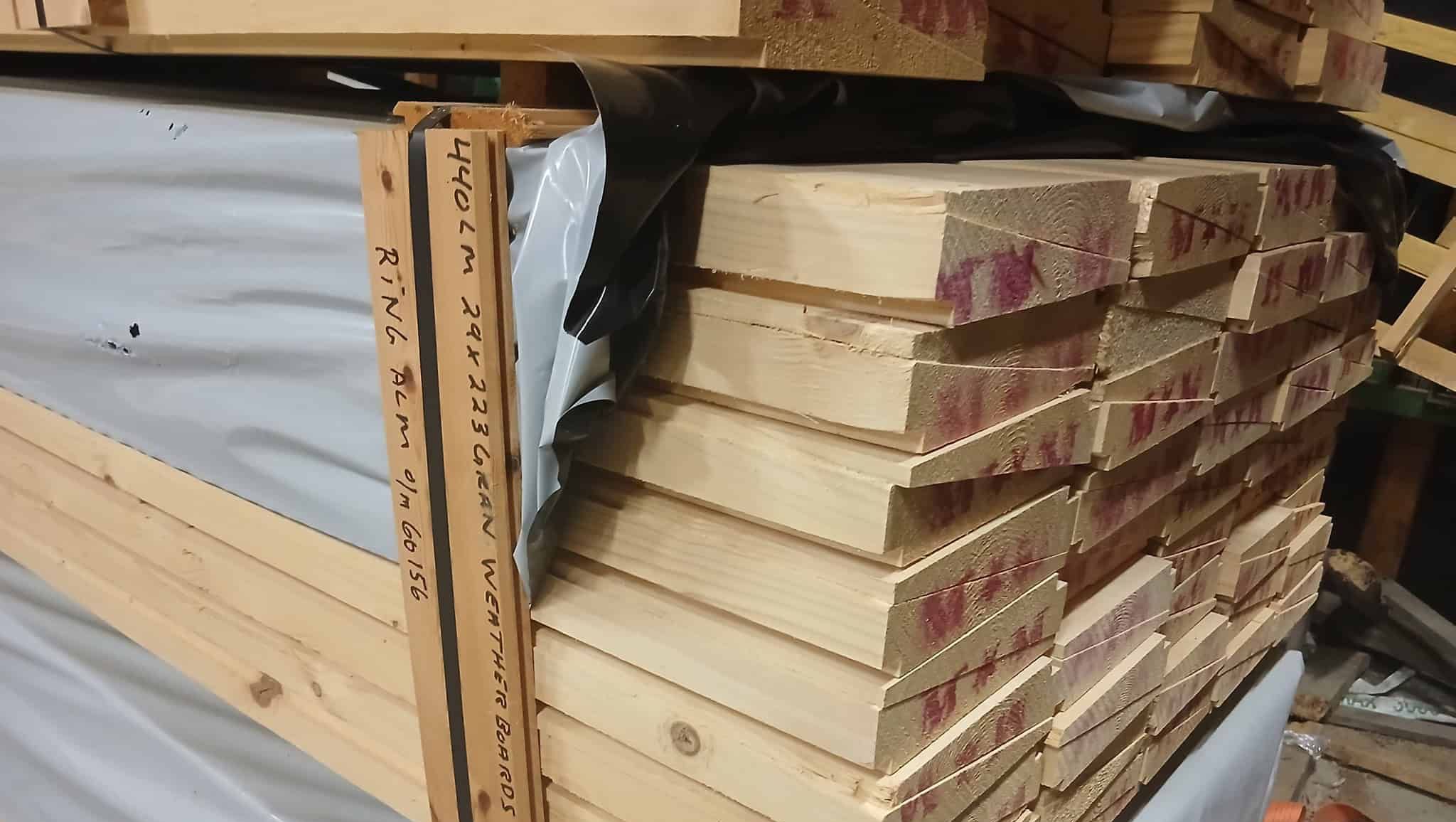 Stablede trebord i furu med not og fjær lagret på pall i verksted.